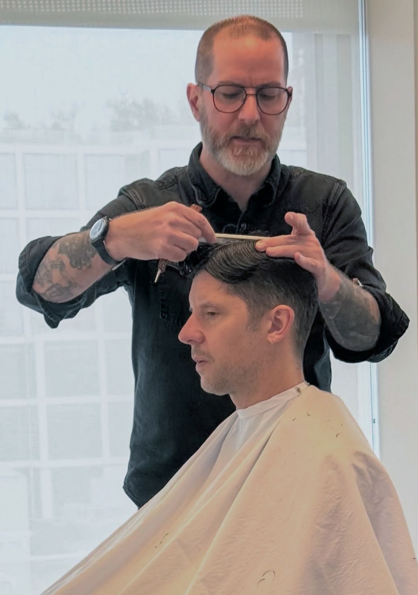 David mid-cut, scissor-over-comb on a client at the salon chair.