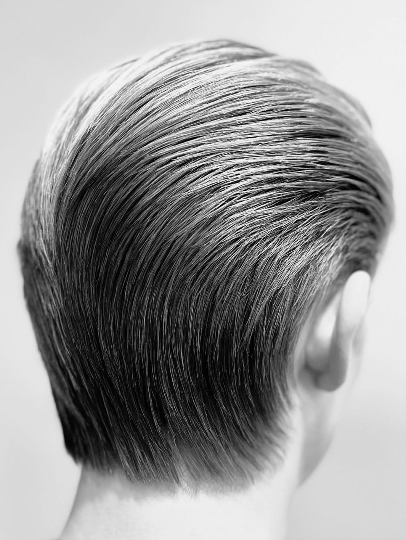 Slicked-back men’s cut seen from behind, clean tapered nape, black-and-white.